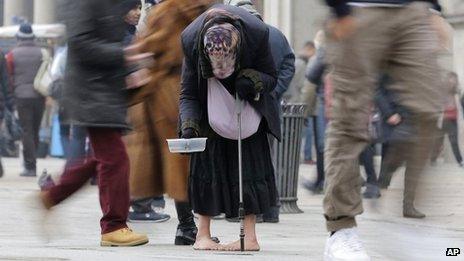 A woman begs for money amid passers by in central Milan, Italy, on 8 January 2013