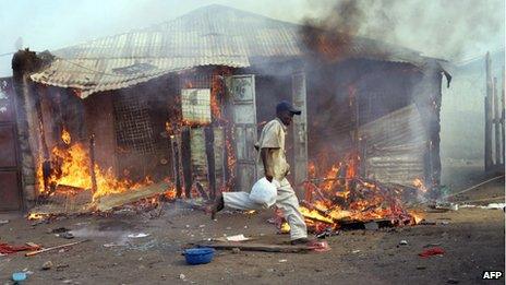 A man runs past a house on fire in Kenya in January 2008