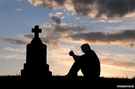 Silhouette of man, sitting contemplatively near a gravestone