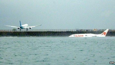 The crashed jet lies in water as another plane lands at Denpasar airport, Bali, 13 April