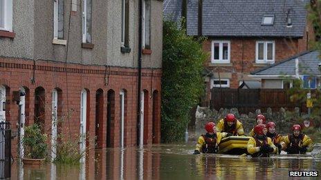 Firefighters pull a boat as they wade down a flooded street in St Asaph