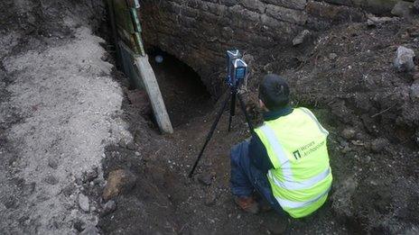 An archaeologist at the entrance of the tunnel uses a laser scanner