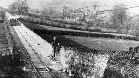 Two children sit on a wall waiting for a train in this black-and-white postcard from the 1930s.