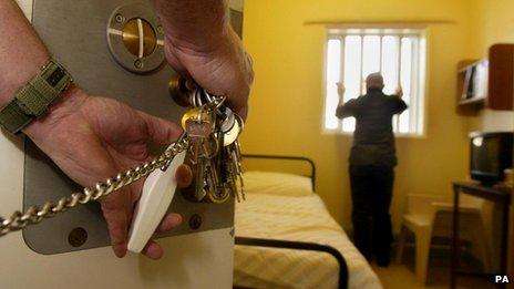 A prison officer unlocks a cell to find a prisoner looking out from a barred window