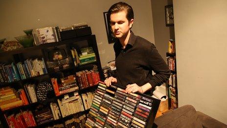 Man holds up a rack of cassette tapes.