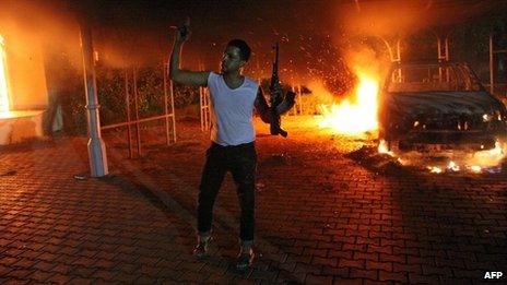 An armed man waves his rifle as buildings and cars are engulfed in flames after being set on fire inside the US consulate compound in Benghazi late on 11 September 2012