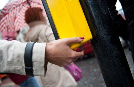 Pedestrian with hand on rotating cone at a pelican crossing