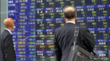 Businessmen look at a share prices board on a window of a securities firm in Tokyo