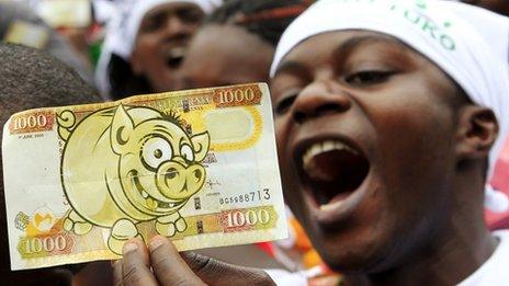 A protester displays a modified Kenyan bank note imprinted with an image of a pig in Nairobi during 11 June 2013