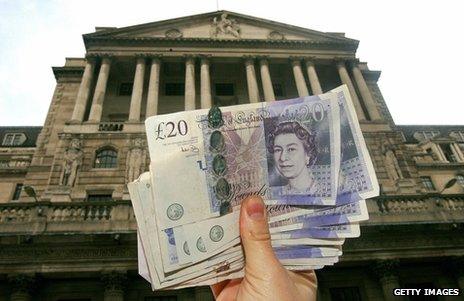 Hand holding up pounds in front of the Bank of England