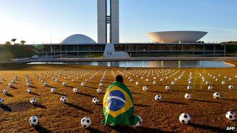 A man with a Brazilian flag crouches among the footballs placed in front of the National Congress building in Brasilia on 26 June 2013