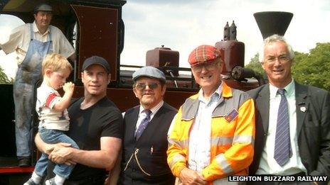 John Travolta holding his son with railway staff in front of a steam train