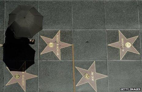 A tourist holding an umbrella to shield herself from the sun walks on Hollywood Walk of Fame stars during a major heat wave in Southern California on Friday