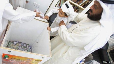 Kuwaiti former MP al-Sawagh helps a Kuwaiti child toss a donation into a wooden box designated to support the Syrian Opposition (27 June 2013)