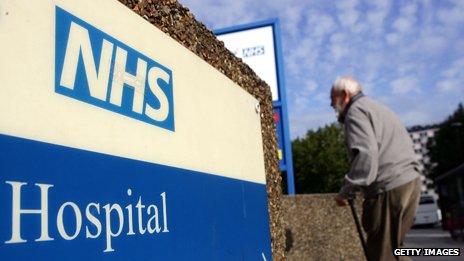 An elderly man walks past an NHS sign