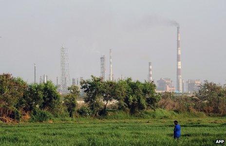 In this photograph taken on April 22, 2013, an Indian man stands in a field as factory chimneys from an industrial area loom in the background in Mumbai.