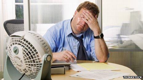 A man sweating while working in an office with a small fan