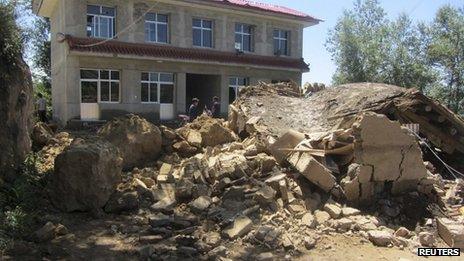 People stand next to a collapsed house after an earthquake struck Minxian county of Dingxi, Gansu province, 22 July 2013