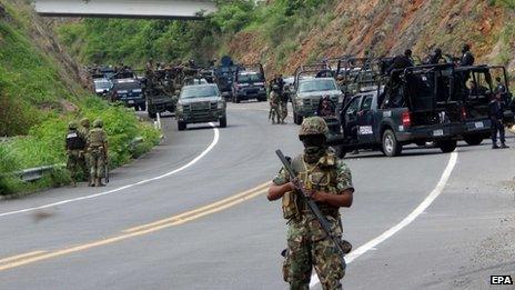 Federal agents and soldiers stand guard on a road in Michoacan after clashes with members of a drug cartel