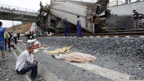 An injured man sits by the track looking at a body covered with a blanket