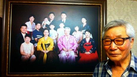 Kim Kyo-yong stands in front of a photo of his South Korean family