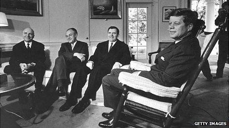 President John F Kennedy sitting in a big rocking chair while three Russian officials sit lower on a couch