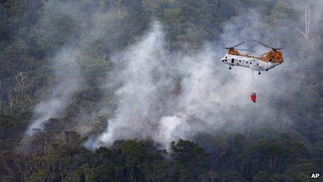 Smoke billows from the crash site of US air force rescue helicopter HH-60 at Camp Hansen as US marine helicopter CH46 flies over to extinguish the fire, in Okinawa, Japan, 5 August 2013