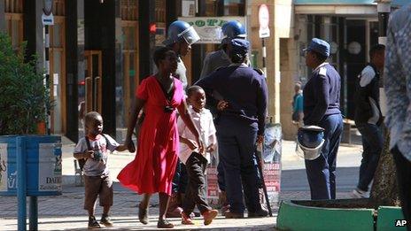 A woman and her children walk past Zimbabwean police in Harare