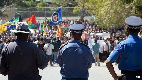 Papua New Guinea police officers watch as hundreds of students march towards the university gate in Port Moresby on 2 August 2013, during a protest rally against Australia and PNG's asylum seeker plan