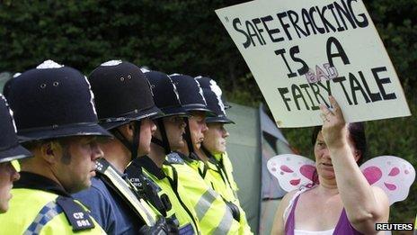 A protester waving an anti-fracking placard greeted by a line of police