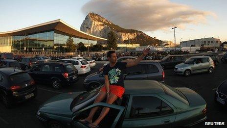 A man sits on his car roof with the Rock of Gibraltar in the background