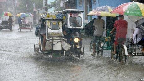 Residents commute along a flooded stretch of road during heavy rain in the suburbs of Manila on 12 August 2013
