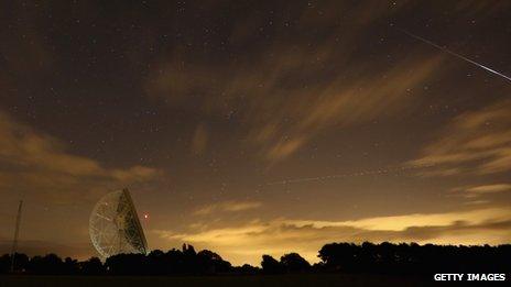 Perseid meteor streaks across the sky past the light trail of an aircraft over the Lovell Radio Telescope at Jodrell Bank in Holmes Chapel