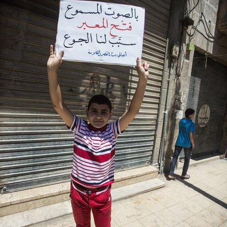 Boy holds placard demanding that the crossing point be closed