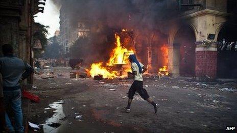 A supporter of the Muslim Brotherhood runs past a burning vehicle during clashes with security officers close to Cairo's Ramses Square (16 August 2013)