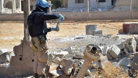 A member of a UN investigation team takes samples of sands near a part of a missile in the Damascus countryside of Ain Terma, Syria, on Wednesday, in an image provided by the United media office of Arbeen