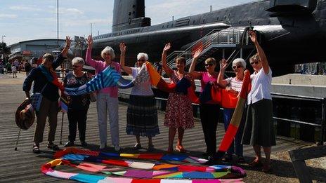 Local knitting group Priddys Purlers revealing part of the giant scarf in front of HMS Alliance