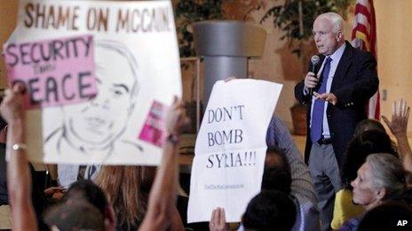 Members of the crowd hold up signs against military action in Syria as US Senator John McCain speaks in Phoenix, Arizona, on 5 September 2013