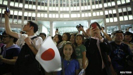 Girl waves Japan's national flag as visitors take photos during an event titled "Tokyo 2020 Host City Welcoming Ceremony