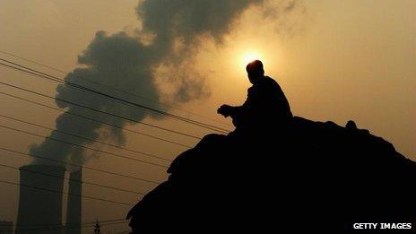 A Chinese man squats on a truck near a power plant emitting plumes of smoke from industrial chimneys on October 30, 2007 in Beijing China.