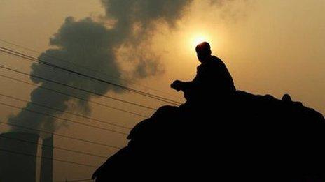 A Chinese man squats on a truck near a power plant emitting plumes of smoke from industrial chimneys on October 30, 2007 in Beijing China.