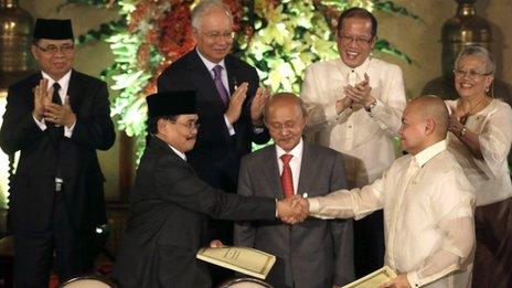 Philippine government peace negotiator Marvic Leonen, right, and Moro Islamic Liberation Front chief negotiator Mohagher Iqbal, left, shake hands as they exchange signed documents of their tentative peace agreement following a formal signing ceremony at Malacanang Palace in Manila, Philippines as Malaysian peace broker Dato Tengko Abdul Ghafar, centre, and others, second row from left, MILF Chair Al Haj Murad, Malaysian Prime Minister Najib Razak, Philippine President Benigno Aquino, and Government peace negotiator Teresita Deles look on and applaud