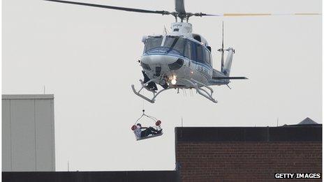 A person is carried by helicopter away from the navy building