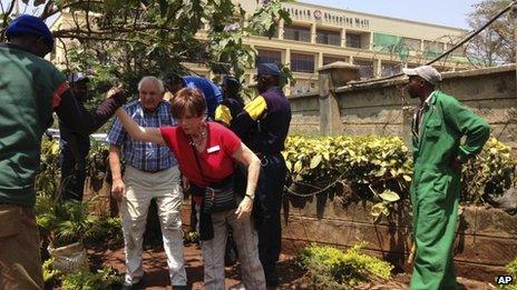 Shoppers are helped to evacuate the area of an upmarket shopping mall, seen background, in Nairobi, Kenya Saturday 21 September 2013.