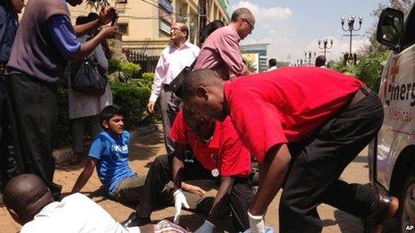 An injured man is treated outside an upmarket shopping mall, seen background, in Nairobi, Kenya, 21 September 2013.