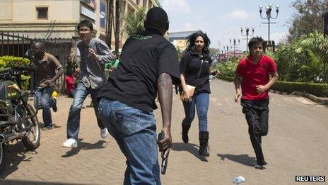 People running towards an armed security officer outside the mall