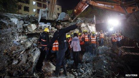 A rescue worker calls for a stretcher as others search for survivors at the site of a collapsed residential building in Mumbai