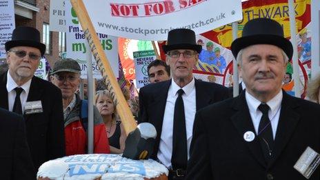 Protesters carrying a "Happy Birthday NHS" cake with a privatisation sledge hammer crushing it.