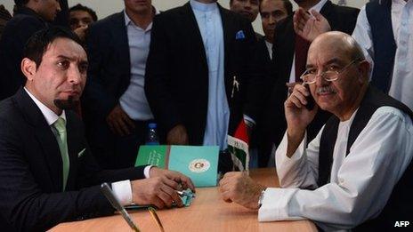 Qayum Karzai (R), the elder brother of Afghan President Hamid Karzai, talks on the phone as he registers his name for the forthcoming presidential elections at the Independent Election Commission (IEC) in Kabul on October 6, 2013.