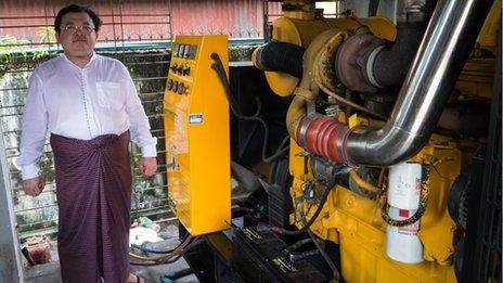 Khin Maung Aye standing next to generators